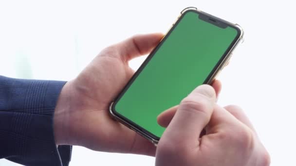 Hombre que utiliza el teléfono inteligente en el espacio de oficina, sentado en la silla y el uso de la maqueta de teléfono de pantalla verde, croma clave, contenido de navegación, video, blogging, tocando el centro de la pantalla, volteando a través de folleto de noticias. — Vídeos de Stock