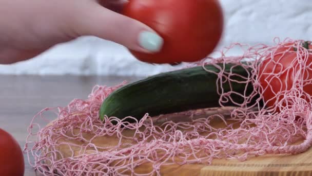 A woman takes out cucumber tomatoes from a reusable grocery bag vegetables on a table in the kitchen at home after shopping for groceries. Waste-free and plastic-free concept. Mesh cotton shopper. — Stockvideo