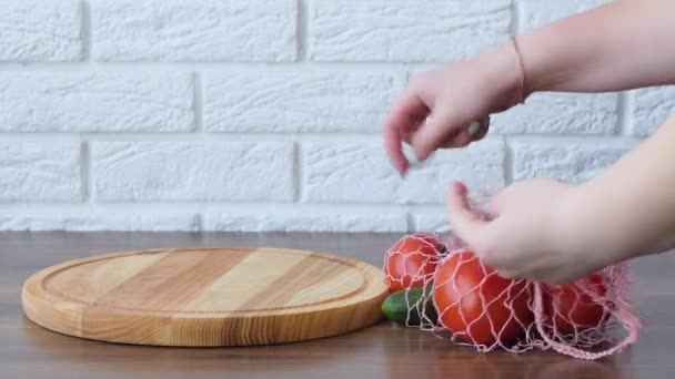 A woman takes out cucumber tomatoes from a reusable grocery bag vegetables on a table in the kitchen at home after shopping for groceries. Waste-free and plastic-free concept. Mesh cotton shopper. — 비디오