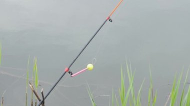 A colored rattle for biting is put on a fishing rod while fishing. Bite signal at the tip of the rod. The bite alarm will alert you to a bite. Fishing tackle close-up.