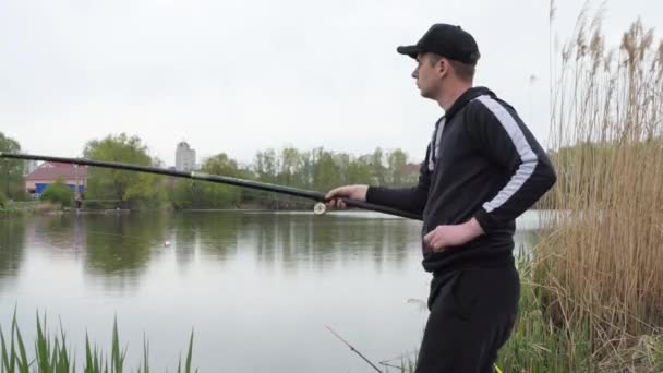 男魚,大規模で穏やかな湖の海岸に立って、釣竿で魚をキャッチし、回転.男は回転棒を穏やかな水面に投げ込んだ。. — ストック動画