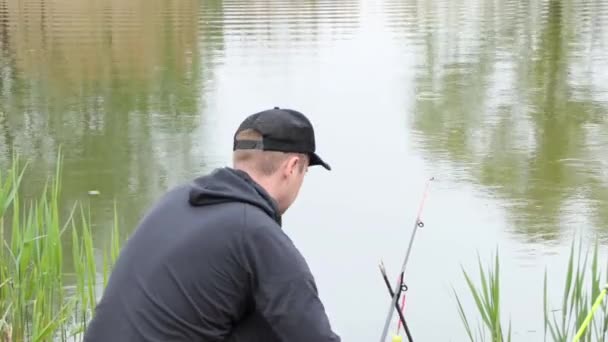 一个人在一个平静的大湖畔钓鱼，用钓竿和纺纱钓到鱼。那个人把纺锤扔进平静的水面. — 图库视频影像