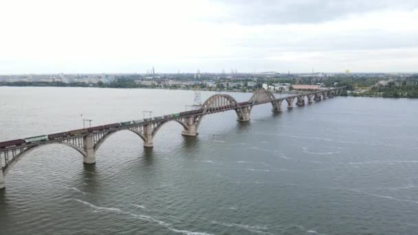 Güzel bir köprüden geçen trenin havadan görünüşü. Yük treni demiryolu köprüsü boyunca ilerliyor. Dnipro şehrindeki eski kemerli Merefo-Kherson köprüsünün havadan görüntüsü.. — Stok video