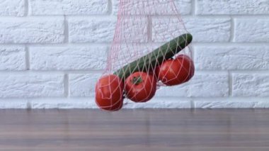 Bir kadın, alışveriş yaptıktan sonra evdeki mutfaktaki bir masada bulunan sebzelerden salatalık domateslerini çıkartıyor. İsrafsız ve plastiksiz konsept. Pamuk tüccarı..