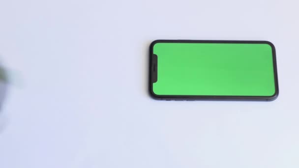 Place for tea drinking with smartphone on white table with green screen. Green tea in a glass cup. Close-up of mobile phone on white table with chroma key, green screen phone and top view — Stock video
