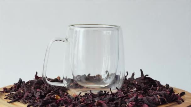 Chá vermelho em uma xícara de vidro em um fundo branco. O chá de hibisco vermelho é derramado em um vidro transparente com paredes duplas. Uma xícara de chá girando em uma placa de madeira. — Vídeo de Stock