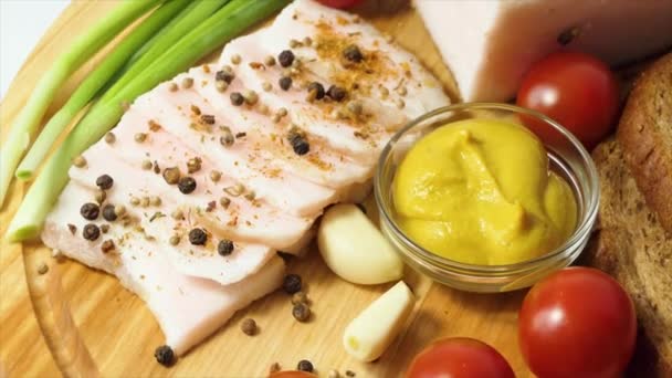 Chopped lard on a board with spices, pepper, mustard, cherry tomatoes, garlic, green onions, black bread. The appetizer pork fat revolves on the board. Close-up — Vídeo de Stock