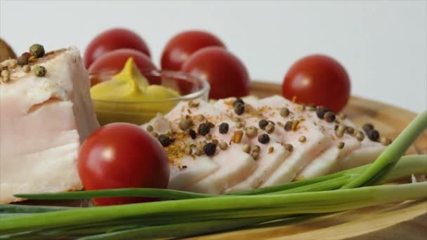 Нарізаний салат на дошці зі спеціями, перцем, гірчицею, вишневими помідорами, часником, зеленою цибулею, чорним хлібом. Закуска свинячого жиру обертається на дошці. Крупним планом — стокове відео