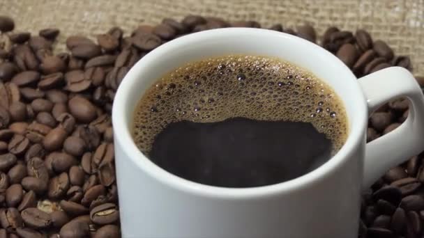 Vit kopp med kaffe på bakgrunden av färska rostade kaffebönor — Stockvideo
