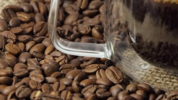 Kopp kaffe med färska rostade kaffebönor bakgrund. En fylld transparent espressokopp med en stor hög med rostade kaffebönor i bakgrunden. — Stockvideo