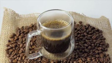 Taze kahve arkaplanlı bir fincan kahve. Şeffaf bir espresso fincanı ve arka planda bir yığın kavrulmuş kahve çekirdeği..