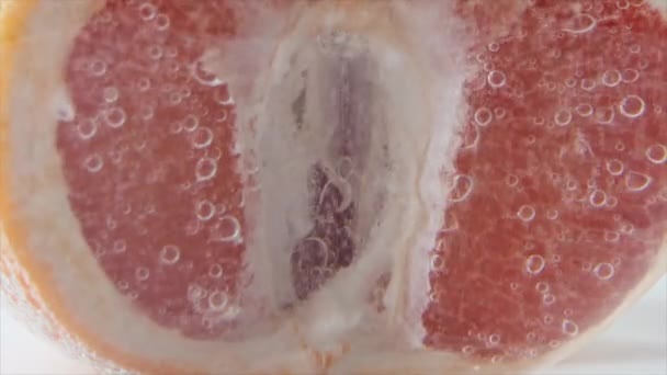 Grapefruit close-up sijpelt of drijft naar de oppervlakte. De helft van de roze grapefruit valt in het water. — Stockvideo