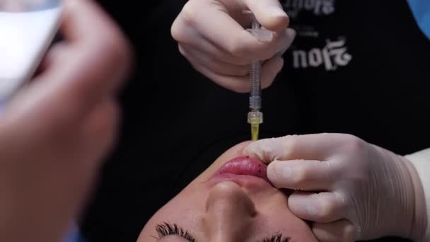 Chirurg, w rękawiczkach medycznych, przekłuwa wargę kobietom strzykawką i powoli wstrzykuje hialuroniczne — Wideo stockowe