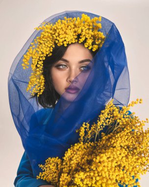 Mavi ceketli ve şallı genç kız stüdyoda bir buket mimoza ile 