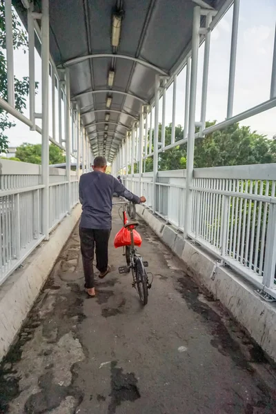 Cakarta, Endonezya, 24 Mart 2022: Arkadan bakıldığında, bir adam sabahın erken saatlerinde Jalan Kyai Tapa, Jakarta, Endonezya 'da yaya geçidinde bisikletine rehberlik ediyor..