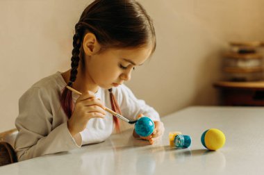 Ukraynalı bir kızın portresi. Çocuk yumurtayı mavi ve sarıya boyar. Çocuk ülkesini seviyor ve destekliyor. Paskalya yumurtalarını mavi ve sarı renklerle boyayan şirin bir kız çocuğu. Paskalya yumurtası taşıyan bir kızın elleri. Yakın plan..