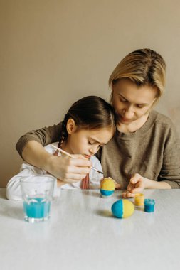 Portrait of a mother and daughter painting an egg in blue and yellow. Ukrainian family is preparing for Easter. The egg is painted in the color of the flag of Ukraine.