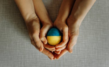 Ukraynalılar Ukrayna bayrağının renklerine boyanmış bir yumurtayı dikkatle ellerinde tutuyorlar. Anne ve çocuk yumurtayı mavi ve sarıya boyadılar. Üst görünüm.