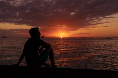 Rahatlatıcı ve mutlu tatili boyunca sahilde doğayı yansıtan ve düşünen genç bir adam silueti. Yaşam tarzı konsepti