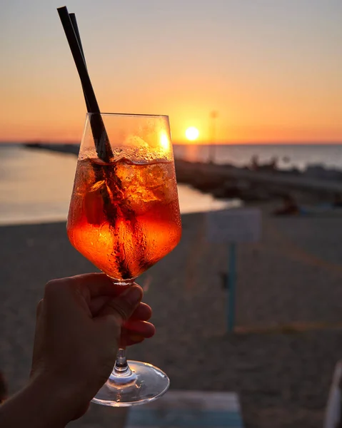 Unrecognizable woman holding a glass of Spritz traditional cocktail with alcohol at a beach bar. European summer drink. Italian drink. Lifestyle concept