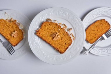 Slices of homemade carrot cake with sugar glaze and walnuts served in three white dishes. Food concept