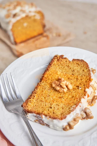 Slice of homemade carrot cake with sugar frosting and nuts on a white plate. Food concept