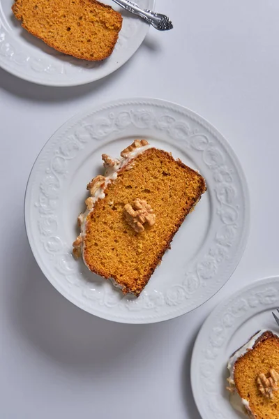 Slices of homemade carrot cake with sugar glaze and walnuts served in three white dishes. Food concept