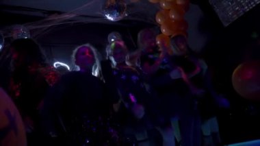 Sochi, Rusya - 01 Kasım 2020: Karanlık gece kulübünde dans eden bir grup genç. Cadılar Bayramı partisi konsepti. Balonların ve neon ışıklarının siyah arkaplanı. Yavaş çekim.