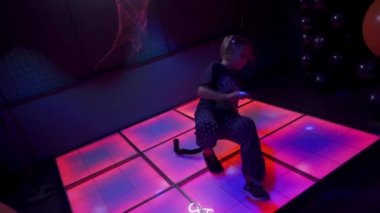 Sochi, Rusya - Kasım 01 2020: Kedi kulakları ve kuyruk dansı yapan küçük kız renkli bir sahnede dans ediyor. Çocuklar için gece kulübünde balonlu ve örümcek ağlı Cadılar Bayramı partisi.