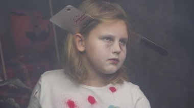 Kafkasyalı sarışın genç adamın yakın plan portresi siyah arka planda korkunç makyajı olan bir zombi gibi kostüm giyiyor. Çocuğun kafası, üzerinde kan damlaları olan bir baltayla delinmiş. Cadılar Bayramı partisi.