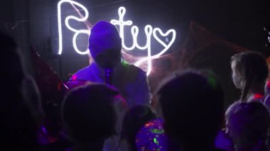 Beyaz mumya kostümü içinde tanınmayan bir adam çocukları eğlendiriyor, mikrofonla konuşuyor, karanlık bir gece kulübünde Cadılar Bayramı etkinliği düzenliyor. Tatil konsepti. Kapalı gece hayatı.