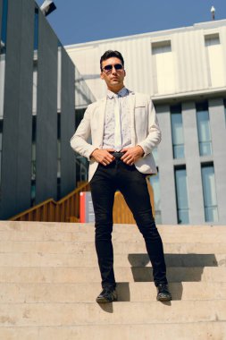 İki renkli kot pantolonlu, siyah beyaz kravatlı ve gözlüklü bir adam..