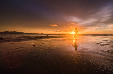 Gün batımında sahilde bir kadının silueti.