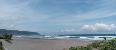 Mavi gökyüzünde, kumsalın tepesinde kahverengi renkli kum ve deniz kenarında kumsal bitkisi olan kara bulutlu bir manzara.