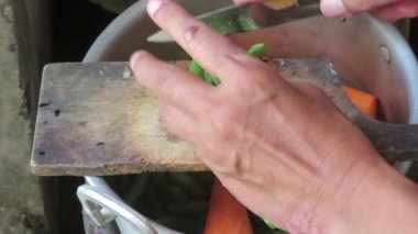 old lady slicing  chickpeas in wooden dirty choping board in the pan