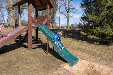 Küçük çocuk baharda dışarıda oyun parkında eğleniyor. ahşap kaydırak.