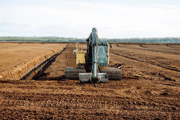 Excavator digging drainage ditch in peat extraction site. Drainage of peat bogs and destruction of trees. Drilling on bog for oil exploration. Wetlands declining and under threat. Mining on peatlands.