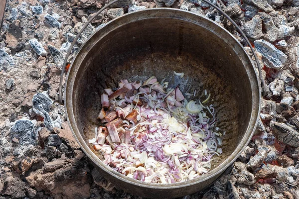 soup cooking process on charcoal. roasting smoked meat and onions in a pot. country kitchen.