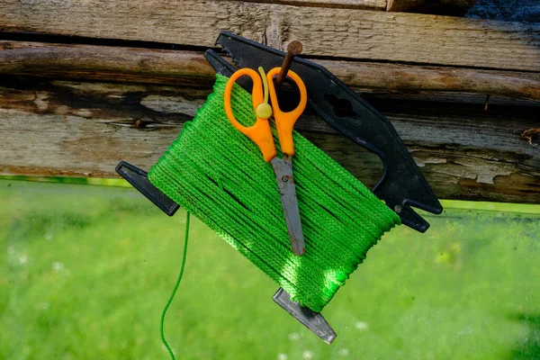 Green garden string on a spool and scissors with orange handles hung on a nail