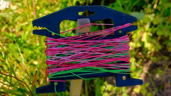 Colorful garden string on a spool and scissors with orange handles hung on a nail.