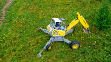 a small yellow excavator digs a stormwater drain at the foot of a hill.