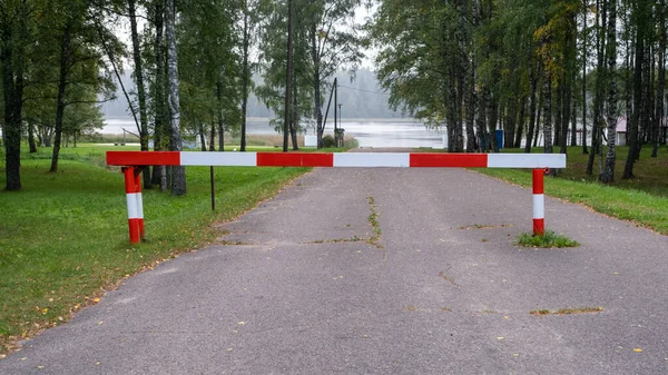 Entry is prohibited. Red and white barrier on the road. The road leads to the lake.