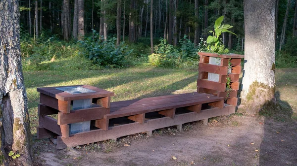 Bench made of windows. Wooden bench in a summer park. Sunny day in the forest on the nature. Wood decor. Trash bin or container near the bench.