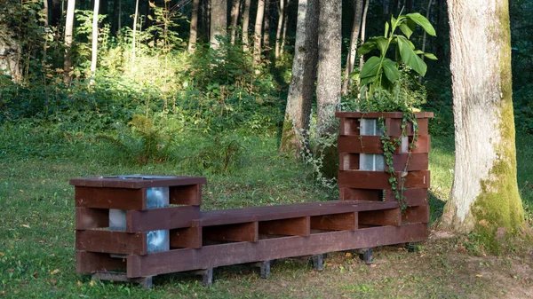 Bench made of windows. Wooden bench in a summer park. Sunny day in the forest on the nature. Wood decor. Trash bin or container near the bench.