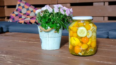 Cam kavanozda konserve ve konserve domatesler. Ev yapımı sebze turşusu. Sağlıklı mayalanmış yiyecek. Sarı domatesler. Kahverengi ahşap bir masada turşulu domates kavanozu. Dekoratif bir saksıda sonbahar çiçekleri