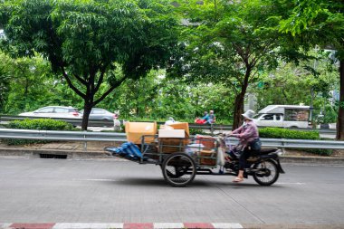 Bangkok, Thailand - August 19, 2022 : Old man on a three-wheel modified motorbike moving in fast, blurred motion. Driver carries recycling selling to the factory.
