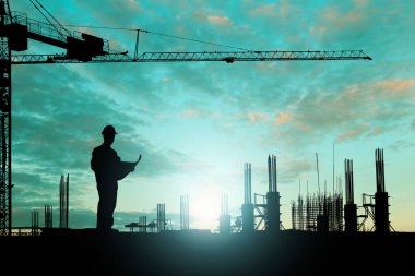Siluet mühendisi gün batımında inşaat işçileri üzerinde çalışırken inşaat planını okuyor. Parlayan ışıklarla yeşil bir arka plan, endüstriyel konsept..