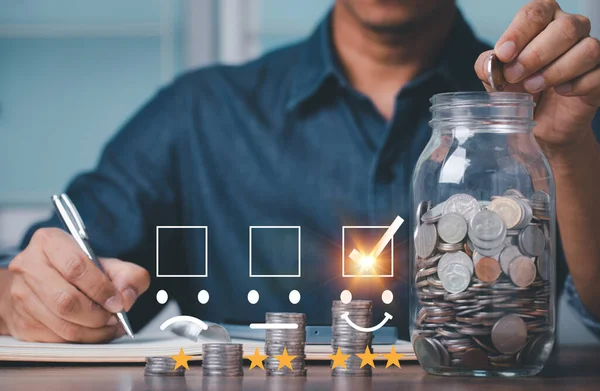 Hand of businessman holding coins putting in glass and documentation in account book. concept saving money for finance accounting. giving satisfaction rating with smile icon and tree stars.
