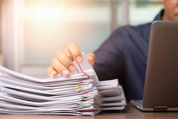 Businessman hand pick up Stack overload documents report paper with colorful paperclip with fair light to analyze data, business and paperless concept.