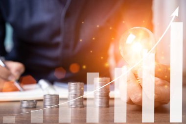 Arka planda para ve notlar olan ampulü tutan bir adam. konsept tasarruf para, elektrik tasarruf